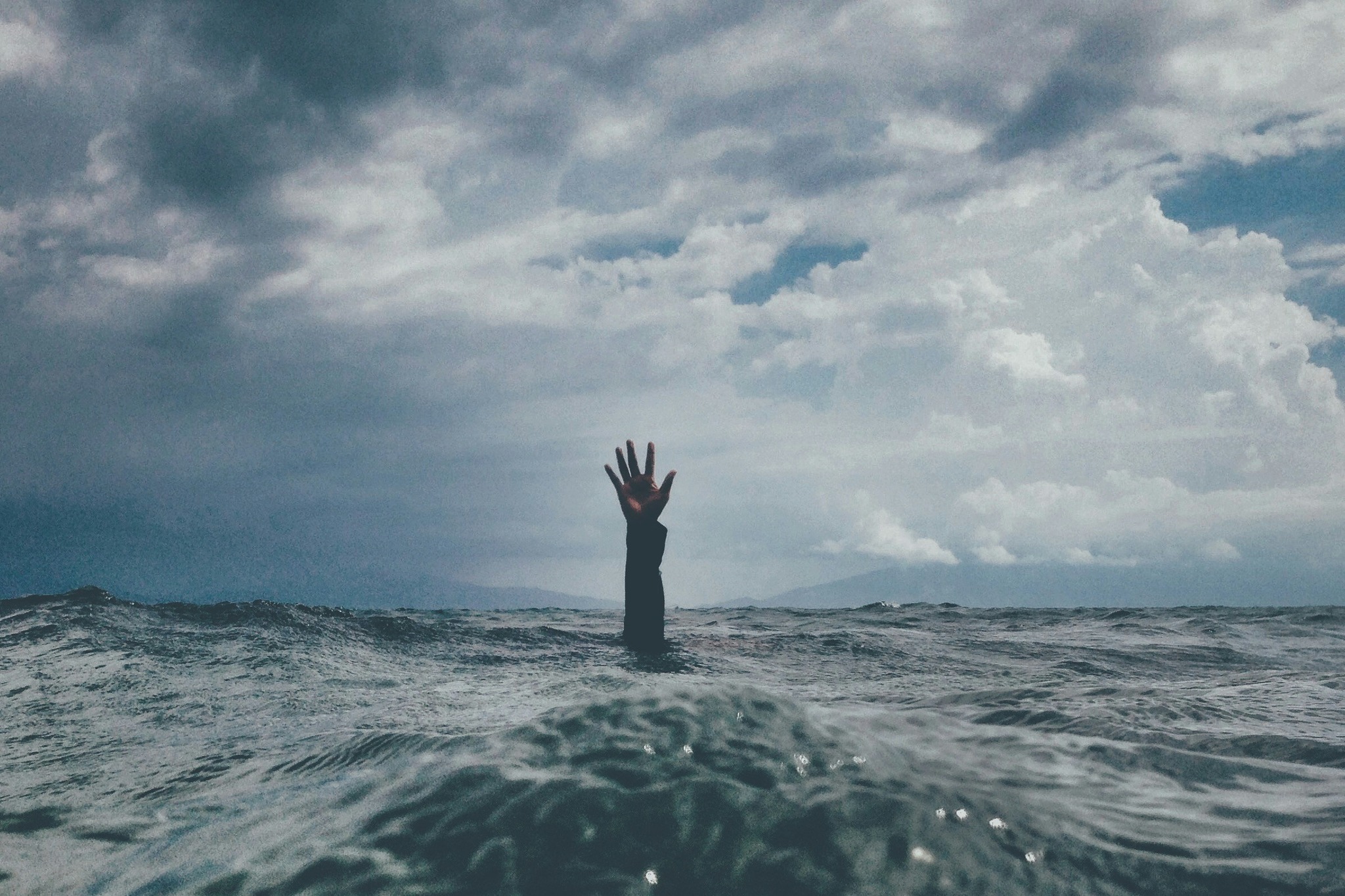 A hand and arm reaching out of rough waters with a stormy sky in the background, symbolizing the struggle of addiction and the need for trustworthy support.